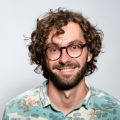 A man with curly hair and glasses smiling for the camera.